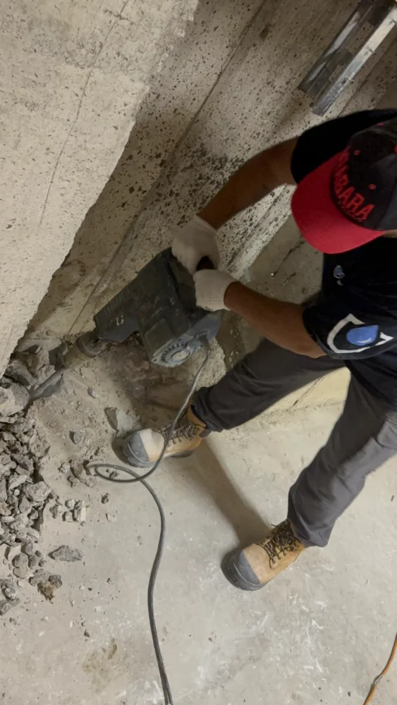 Contractor using a jackhammer for concrete floor demolition during interior waterproofing in Aurora.
