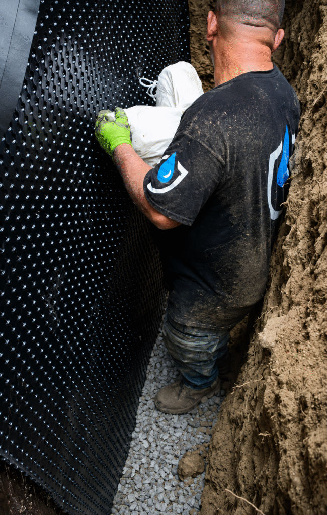 Waterproofing technician installing a heavy-duty dimpled drainage membrane along the foundation wall in Ajax.