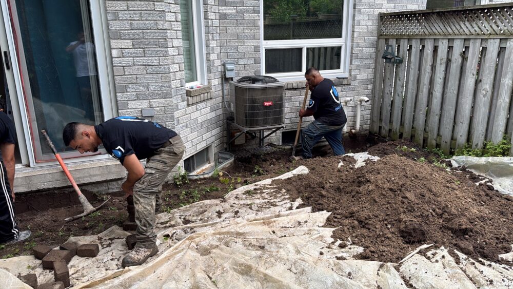 DGI Waterproofing crew performing manual exterior excavation near a leaking basement window in Ajax.