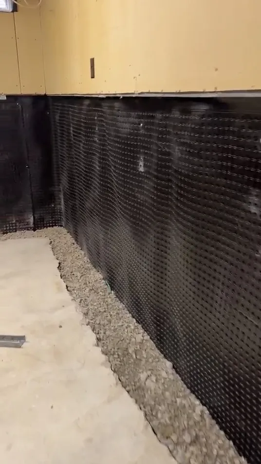 Installed interior dimpled drainage membrane and clear gravel along a basement wall in Aurora.