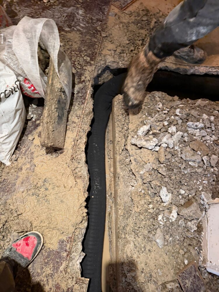 Contractor installing black weeping tile in a muddy basement trench to relieve hydrostatic pressure in Pickering.