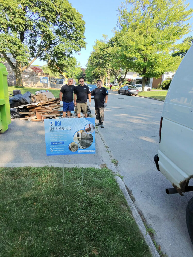 The DGI Waterproofing expert contractor team standing next to their company sign and demolition debris after completing an emergency basement repair in North York.