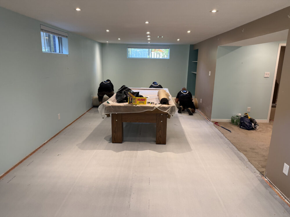 DGI Waterproofing team rolling up wet carpet and subflooring around a pool table to prepare for interior waterproofing in a North York home.
