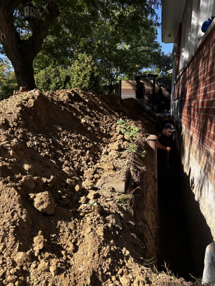 Waterproofing contractor working inside a deep exterior foundation trench to perform professional crack repair and waterproofing in Toronto.