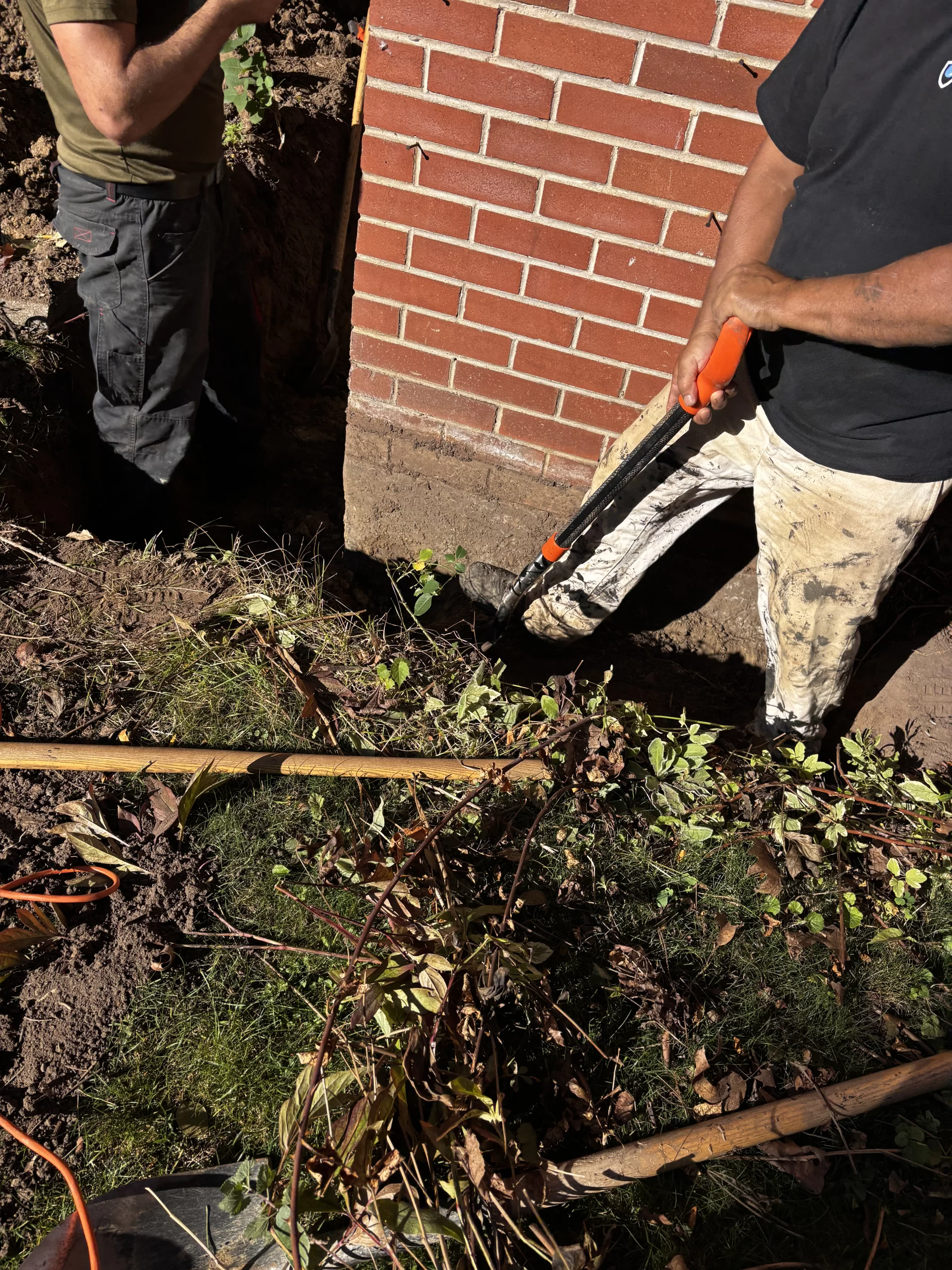 A DGI Waterproofing specialist manually excavating soil along a brick foundation wall to prepare for exterior waterproofing in Toronto