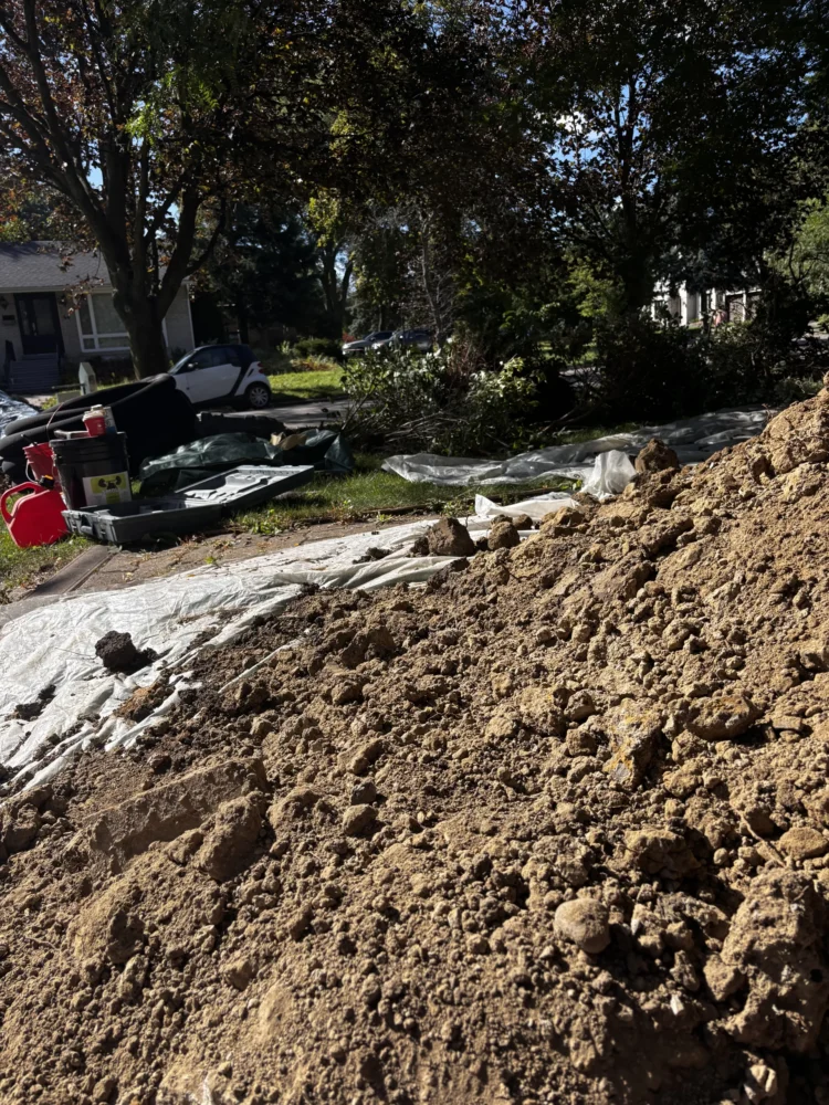 Excavated soil safely placed on protective tarps to preserve the homeowner's lawn during a Toronto exterior waterproofing project.